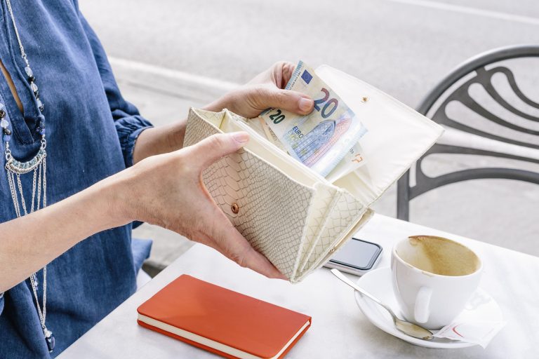 Hand of senior woman removing euro note from purse at sidewalk cafe